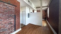 Located at 402 North 18th Street in Richmond, Virginia, this unit offers an intimate yet characterful living space spread across a single floor. The interior immediately draws the eye with its striking exposed brick walls, a hallmark of the building's historic industrial roots, which appear throughout the main room and hallway, adding warmth and texture to the space.

Hardwood-style flooring runs throughout, lending a cohesive and clean aesthetic that complements the raw brick surfaces. The main room benefits from a window that invites natural light and frames outdoor views of the surrounding Richmond landscape, creating a bright and airy atmosphere despite the compact footprint. Exposed concrete structural elements and visible ductwork overhead reinforce the loft-like, urban character of the unit.

A hallway connects the main living area to the remaining rooms, including a closet that offers practical storage. The bathroom is neatly appointed with tile flooring, a combination bathtub and shower, a toilet, and a vanity featuring wood cabinetry topped with a dark granite-style surface — providing a functional and tidy finish.

The overall ambiance of this space is one of urban industrial charm, where the building's historic bones are thoughtfully preserved alongside clean, updated finishes.