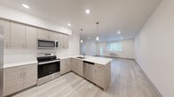 Located at 12608 E Nora Ave in Spokane Valley, WA, this thoughtfully designed 2-bedroom, 2-bathroom unit offers a clean, contemporary aesthetic throughout. The open-concept kitchen and living area serves as the heart of the home, showcasing light wood-grain cabinetry, crisp white quartz countertops, and a peninsula island with an undermount sink and pendant lighting overhead. Stainless steel appliances — including a refrigerator, electric range, microwave, and dishwasher — complete the modern kitchen. Light wood-style plank flooring flows seamlessly through the main living area, enhancing the bright and airy atmosphere created by recessed lighting and large windows that invite natural light. The living room provides access to a private balcony with outdoor views, adding an appealing extension to the main living space. Both bedrooms feature neutral wall tones and plush carpeting, each with windows dressed in horizontal blinds. The bathrooms are finished in a clean, minimalist style, with one featuring a full soaking tub and shower combination. The overall design emphasizes a fresh, modern sensibility with a light, neutral palette that creates a welcoming and versatile living environment.