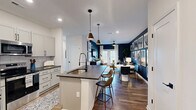 Located in Huntersville, NC, this well-designed two-bedroom, two-bathroom home offers a thoughtful single-floor layout that maximizes comfort and functionality. The open-concept kitchen and living area serves as the heart of the home, anchored by a large central island with dark quartz countertops, bar seating, and stylish pendant lighting. White shaker cabinets, a subway tile backsplash, and a full suite of stainless steel appliances give the kitchen a clean, modern aesthetic. Hardwood-style flooring flows throughout the entire home, adding warmth and continuity. The living room makes a bold statement with deep navy accent walls, French doors that invite natural light, and a ceiling fan overhead. The primary bedroom continues the navy palette with a dramatic accent wall, creating a cozy yet sophisticated retreat, complemented by a spacious walk-in closet with wire shelving. The second bedroom features a contrasting painted ceiling and generous natural light. Both bathrooms are well-appointed, with one featuring a sleek sliding glass walk-in shower, dark-framed fixtures, and granite-topped vanities with gray cabinetry. Two closets provide ample storage throughout the home, rounding out this move-in-ready residence.