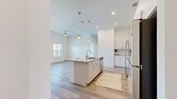 This well-appointed 3-bedroom, 2-bathroom residence offers a thoughtfully designed single-floor layout with a clean, modern aesthetic throughout. Light-toned hardwood flooring flows seamlessly across all rooms, creating a bright and cohesive feel.

The open-concept kitchen serves as the heart of the home, centered around a granite-topped island with an integrated sink and pendant lighting overhead. White shaker-style cabinetry extends to the ceiling, complemented by a subway tile backsplash and a full suite of stainless steel appliances including a refrigerator, range, microwave, and dishwasher. The kitchen opens directly to the living area, making it ideal for entertaining.

The bedrooms are generously proportioned, featuring tall ceilings, ceiling fans, and large windows that invite natural light and offer outdoor views of the surrounding neighborhood. The primary bedroom includes a spacious walk-in closet with dual hanging rods and built-in shelving. Two additional closets elsewhere in the home provide ample storage.

The bathrooms are finished with elegant marble-style tile surrounds on the soaking tub and shower areas, paired with chrome fixtures for a polished look. The entrance provides a welcoming transition into the main living spaces. Overall, the residence presents a bright, neutral palette with modern finishes throughout.