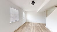 This thoughtfully updated two-floor space showcases a clean, modern aesthetic defined by crisp white walls, light-toned hardwood-style flooring, and contemporary black hardware and fixtures carried consistently throughout. The open layout is accentuated by abundant natural light streaming through multiple windows fitted with horizontal blinds, creating a bright and airy atmosphere across both levels.

The kitchen is a standout feature, offering white shaker-style cabinetry with matte black hardware, granite countertops with subtle grey and white veining, a classic white subway tile backsplash, a stainless steel double-basin sink, and stainless steel appliances including a dishwasher. The bathrooms echo this refined palette, featuring granite-topped vanities, white cabinetry, round frameless mirrors, and sleek black accent fixtures and lighting.

The living and bedroom areas are generously proportioned, each benefiting from natural light and the warmth of the continuous light wood flooring. A staircase connects the two floors seamlessly. A dedicated laundry area with a stacked washer and dryer adds valuable in-unit convenience. Throughout the space, the minimalist design language, consistent material choices, and attention to detail create a cohesive, move-in-ready environment well-suited for modern living.
