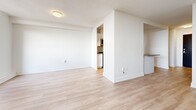Located at 580 The East Mall in Toronto's Etobicoke neighbourhood, this single-floor unit offers a clean, modern aesthetic throughout its thoughtfully organized layout. Light-toned laminate flooring flows continuously through the living area, hallway, and kitchen, creating a cohesive and airy feel. Crisp white walls and bright finishes reflect natural light effectively throughout the space.

The living area is generously proportioned, featuring a large window that allows abundant natural light to fill the room and offers views of the surrounding area. A baseboard heating unit runs along the exterior wall beneath the window, ensuring year-round comfort.

The kitchen is efficiently designed with white cabinetry, dark countertops, and a full suite of stainless steel appliances, including a French door refrigerator, over-the-range microwave, and electric range. A peninsula counter separates the kitchen from the living space, providing additional prep area and a natural division between the two zones. Track lighting overhead ensures the kitchen is well-lit.

The bathroom features a full soaker tub and shower combination, finished with classic white subway tile extending to the ceiling, creating a clean and timeless look. The hallway entry provides a practical transition point connecting all areas of the unit, completing this well-organized and move-in ready space.