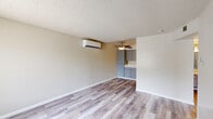 This single-floor unit offers a clean, functional layout with a cohesive neutral color palette and light wood-style laminate flooring that flows seamlessly throughout the space. The open living area is generously sized, featuring a wall-mounted ductless mini-split air conditioning unit for efficient climate control and a ceiling fan that enhances airflow and comfort. Textured popcorn ceilings add a classic character to each room.

The kitchen is well-equipped with ample gray cabinetry — both upper and lower — providing substantial storage, complemented by white tile countertops, a built-in sink, a dishwasher, and a coil-top electric range. A range hood and overhead lighting complete the functional cooking space, which opens conveniently toward the living area.

A dedicated bedroom offers a bright, airy feel thanks to a window with exterior views, while a secondary room near the entry door provides flexible use as an additional bedroom or multipurpose space. The bathroom is neatly finished with a full tub-shower combination, updated chrome fixtures, a vanity with a light countertop, and matching wood-style tile flooring. The entry door opens into a well-lit area, offering a welcoming transition into the home. Overall, the unit presents a tidy, move-in ready environment with practical features throughout.