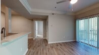This single-floor residence offers a thoughtfully designed layout that maximizes comfort and functionality. The open-concept living area features warm wood-look luxury vinyl flooring, elegant crown molding, and a ceiling fan, creating a bright and welcoming atmosphere. A set of sliding glass doors with vertical blinds opens to an outdoor balcony, allowing natural light to pour in and providing leafy exterior views. The living space flows seamlessly into the kitchen through a pass-through bar counter, making it ideal for entertaining. The kitchen is well-equipped with rich wood cabinetry, speckled stone countertops, a stylish mosaic tile backsplash, black appliances including an electric range, over-the-range microwave, and dishwasher, as well as a deep double-basin stainless steel sink. The bedroom is carpeted for comfort and features a ceiling fan and a window overlooking lush greenery, creating a serene retreat. The bathroom is finished with warm-toned tile flooring, a wood vanity with stone countertops, a single sink, and a shower-tub combination, complemented by neutral gray walls throughout. Crown molding, consistent neutral tones, and quality finishes tie the entire space together with a clean, cohesive aesthetic.