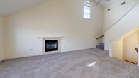 This two-floor residence offers a thoughtfully designed layout with two bedrooms, two full bathrooms, and a loft. The main living area immediately impresses with soaring vaulted ceilings, a tile-surround fireplace, and a striking arched window that floods the space with natural light. A ceiling fan and staircase with wood railing connect the main level to the upper loft. The kitchen is well-equipped, featuring rich cherry wood cabinetry with arched detailing, dark granite countertops, stainless steel appliances including a range, over-the-range microwave, and dishwasher, all set over durable wood-look flooring. Both full bathrooms are finished in clean white tile with pedestal sinks, mirrored medicine cabinets with vanity lighting, and tub-shower combinations. The bedrooms are carpeted and offer ample space, with one bedroom featuring a walk-in closet and direct bathroom access. The loft level, accessible via the main staircase, provides a versatile open space with recessed lighting, sloped ceilings, and a half-wall overlooking the main floor, ideal for use as a home office, study, or additional living area. Soft carpet runs throughout the bedrooms and living spaces, creating a comfortable and cohesive feel.