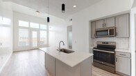 This contemporary single-floor residence showcases a clean, modern design with an open-concept layout that seamlessly connects the kitchen, dining, and living areas. The kitchen is a standout feature, boasting a large quartz-topped island with an undermount sink, gray shaker cabinetry, a white subway tile backsplash, and a full suite of stainless steel appliances including a refrigerator, electric range, and over-the-range microwave. Light wood-style flooring runs throughout the main living areas, complementing the bright, neutral color palette.

The living area impresses with soaring ceilings and a wall of floor-to-ceiling windows and glass French doors that flood the space with natural light and provide outdoor views. A ceiling fan adds both style and function to this expansive area.

The bedrooms are carpeted and well-lit with natural light from windows offering exterior views. One bedroom includes a ceiling fan, while both offer a comfortable, restful atmosphere. Each bathroom is finished with light wood-style flooring, gray shaker vanities with quartz countertops, and tiled shower-tub combinations. One bathroom also features convenient access to a walk-in closet. The overall ambiance is bright, clean, and move-in ready.