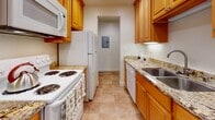 This single-floor unit offers a practical and comfortable layout designed for everyday living. The open living area is finished with plush wall-to-wall carpeting and recessed lighting that creates a bright, welcoming atmosphere. A sliding glass door at one end of the living space provides access to an outdoor area and allows natural light to fill the room.

The galley-style kitchen is efficiently arranged with warm honey-toned wood cabinetry on both sides, granite-look countertops, a stainless steel sink, and a full suite of white appliances including a refrigerator, electric range, microwave, and dishwasher. Tile flooring runs throughout the kitchen, which also features an electrical panel conveniently located in an adjacent alcove.

The bedroom is carpeted and offers ample storage through a built-in sliding-door closet with shelving and hanging rods. A hallway connects the bedroom to the bathroom, which is appointed with a wood-framed vanity, granite countertops, and a mirrored cabinet above the sink. Additional closet storage is accessible along the hallway.

Throughout the unit, clean white walls, consistent trim, and recessed lighting contribute to a neutral and functional aesthetic that provides a versatile canvas for personalization.