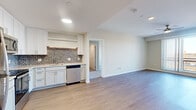 Located at 44 High St in downtown Nashua, NH, this well-appointed 3-bedroom, 2-bathroom residence offers a modern, open layout across a single floor. The combined kitchen and living area serves as the heart of the home, featuring white shaker cabinetry, a mosaic tile backsplash, stainless steel appliances including a refrigerator, range, microwave, and dishwasher, all set above light-toned hardwood-style flooring that flows throughout the main living spaces. The open living area provides a clean, versatile canvas with recessed lighting overhead.

The primary bedroom is a generously sized retreat, highlighted by a large picture window with vertical blinds and a ceiling fan, offering sweeping urban views of the Nashua skyline. The additional bedrooms are carpeted for comfort and also feature ceiling fans and windows with city views, making each room bright and functional. Two walk-in closets with wire shelving provide ample storage.

The bathrooms are finished with gray vanity cabinetry, illuminated mirrors, white countertops, and hardwood-style flooring. One bathroom includes a stacked in-unit washer and dryer, adding everyday convenience. A dedicated walk-in shower with built-in seating completes the second bath. The unit presents a clean, contemporary aesthetic throughout.
