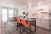 Located at 26701 McBean Pkwy in Santa Clarita, CA, this well-appointed single-floor residence offers a thoughtfully designed open-concept layout that seamlessly connects the kitchen, dining, and living areas. The kitchen is a standout feature, showcasing crisp white cabinetry extending to the ceiling, stainless steel appliances including a gas range, over-the-range microwave, dishwasher, and a side-by-side refrigerator with water and ice dispenser. A classic subway tile backsplash, a stainless steel sink, and light-toned countertops complete the clean, modern aesthetic. The dining area flows naturally from the kitchen, providing an ideal space for everyday meals or entertaining. The living area is bright and welcoming, bathed in natural light from large windows and a glass door that opens to a balcony with outdoor views. Warm wood-look flooring runs throughout the main living spaces, adding cohesion and warmth to the interior. The bathroom features a full tub-shower combination with a stylish striped curtain, a white vanity with storage, built-in wall shelving, and matching wood-look flooring, offering a clean and functional design. The overall ambiance is contemporary and light-filled, with a neutral color palette that creates a versatile and inviting atmosphere.