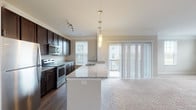 This single-floor residence in Hilliard, Ohio offers a thoughtfully designed layout with modern finishes and a comfortable, open feel throughout. The kitchen is a standout feature, showcasing rich dark cabinetry, granite countertops, stainless steel appliances including a refrigerator, range, and built-in microwave, and elegant pendant lighting. A generous island with an undermount sink provides additional prep space and serves as a natural divide between the kitchen and the open living area. Sliding glass doors in the living area allow abundant natural light and provide access to an outdoor balcony with exterior views. The living space features plush carpeting and crown molding, contributing to a clean, polished aesthetic. The bedrooms are carpeted and well-proportioned, each offering closet storage, including a walk-in closet in the primary bedroom. The primary bathroom features a tiled walk-in shower with a glass enclosure, granite vanity, wood-look flooring, and direct access to the walk-in closet. A secondary bathroom includes a full tub-shower combination, granite vanity, and wood-look flooring. The overall design balances functionality with contemporary style, making this a well-equipped and inviting space.