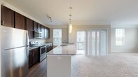This single-floor residence in Hilliard, Ohio offers a thoughtfully designed layout with modern finishes and a comfortable, open feel throughout. The kitchen is a standout feature, showcasing rich dark cabinetry, granite countertops, stainless steel appliances including a refrigerator, range, and built-in microwave, and elegant pendant lighting. A generous island with an undermount sink provides additional prep space and serves as a natural divide between the kitchen and the open living area. Sliding glass doors in the living area allow abundant natural light and provide access to an outdoor balcony with exterior views. The living space features plush carpeting and crown molding, contributing to a clean, polished aesthetic. The bedrooms are carpeted and well-proportioned, each offering closet storage, including a walk-in closet in the primary bedroom. The primary bathroom features a tiled walk-in shower with a glass enclosure, granite vanity, wood-look flooring, and direct access to the walk-in closet. A secondary bathroom includes a full tub-shower combination, granite vanity, and wood-look flooring. The overall design balances functionality with contemporary style, making this a well-equipped and inviting space.
