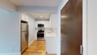 Unit 506 at 5959 Broadway in the Riverdale neighborhood of the Bronx offers a clean, modern living experience defined by quality finishes and a bright, cohesive aesthetic throughout. Warm hardwood flooring extends seamlessly across all living areas, reflecting natural light and lending a polished feel to every room.

The kitchen is a standout feature, showcasing white shaker cabinetry, crisp white quartz countertops, and a classic subway tile backsplash. Stainless steel appliances — including a refrigerator, electric range, and over-the-range microwave — complete the space, making it both functional and visually appealing. The entry foyer flows directly into the kitchen, establishing a welcoming first impression upon arrival.

The bedrooms are generously proportioned, with soft gray-toned walls, recessed lighting, and ample closet space. One bedroom features a dedicated closet with a rod and shelf, while another enjoys a bright window with views of the surrounding neighborhood. Each room offers a calm, neutral palette well-suited for personalization.

The bathroom is fully renovated with white subway tile wainscoting, marble-look porcelain floor tile, a white vanity with brushed nickel hardware, and a mirrored medicine cabinet — delivering a clean, spa-like atmosphere. Overall, this residence presents a move-in-ready space with contemporary upgrades throughout.