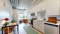 Located at 2650 University Ave SE in Minneapolis, this thoughtfully designed two-bedroom, two-bathroom unit blends modern finishes with an industrial aesthetic across a single floor. The open-concept kitchen, dining, and living area serves as the heart of the home, showcasing soaring concrete ceilings with exposed ductwork and pipes that lend a distinct loft-like character. The kitchen is well-appointed with stainless steel appliances — including a refrigerator, electric range, microwave, and dishwasher — complemented by light wood cabinetry, white countertops, and a single-basin sink. Light wood-style flooring runs throughout the main living areas, enhancing the bright and airy atmosphere. Large windows bring in generous natural light and offer views of the surrounding neighborhood's lush tree canopy. The living area provides a comfortable, open setting that flows seamlessly from the kitchen. Both bedrooms are carpeted and feature windows with outdoor views, with the primary bedroom offering a quiet, private retreat. Each bathroom is finished with light wood-look flooring, clean white walls, and simple modern vanities. Additional conveniences include in-unit laundry and two closets. This unit offers a stylish urban living experience in the vibrant University Avenue corridor.