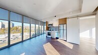 Located at 7 New York Ave NE in Washington, DC, this modern three-bedroom, one-bathroom residence offers a well-designed layout with contemporary finishes throughout. The open-concept living and kitchen area is a standout feature, anchored by dramatic floor-to-ceiling windows that span an entire wall, flooding the space with natural light and framing expansive views of the surrounding DC cityscape. Rich hardwood flooring runs throughout the living area, complementing the clean, modern aesthetic. The kitchen is efficiently designed with white cabinetry accented by warm wood upper cabinets, stainless steel appliances including a refrigerator, microwave, and range, and a sliding barn-style door that adds a stylish architectural detail. The three bedrooms are bright and well-proportioned, each with hardwood floors, neutral walls, and closet space. Sliding frosted-glass barn doors provide flexible room separation in the bedroom corridor, enhancing the open feel. The bathroom is finished with large-format light tile flooring, a sleek vanity with wood accents, a wall-length mirror, and a glass-enclosed walk-in shower. Corner windows in select rooms offer additional city views, making this a light-filled and thoughtfully designed urban residence.
