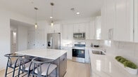 Located at 31601 Gabby Ct in Chesterfield, MI, this well-appointed 2-bedroom, 2-bathroom single-floor home offers a thoughtfully designed open-concept layout filled with natural light. The combined living, dining, and kitchen area forms the heart of the home, anchored by a sleek kitchen showcasing crisp white cabinetry, a striking quartz-topped island with seating for multiple guests, stainless steel appliances, a subway tile backsplash, and elegant pendant lighting above. Light hardwood-style flooring flows throughout, enhancing the bright, airy atmosphere. The living area features a large multi-pane window that frames peaceful views of the surrounding greenery, creating a seamless connection with the outdoors. Both bedrooms are comfortably sized, each offering closet space and windows that invite natural light; the primary bedroom overlooks serene outdoor scenery. The two bathrooms are clean and functional—one includes a glass-enclosed walk-in shower, while the second offers a full shower-tub combo. Four closets provide generous storage throughout. A dedicated utility room and hallway complete the efficient floor plan. The overall ambiance is modern, calm, and cohesive, with a neutral white palette that lends itself to a fresh, move-in-ready feel.