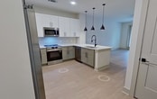 This 820-square-foot, two-bedroom, one-bathroom apartment at 13111 Tadeo Drive, Apt 1235, Charlotte, NC 28078 offers a modern open-concept layout with consistent light wood-style flooring and a neutral color palette throughout. The kitchen is a standout feature, showcasing two-tone cabinetry with sage green lower cabinets and white uppers, white quartz countertops, a subway tile backsplash, and stainless steel appliances including a range, microwave, and French door refrigerator. A kitchen island with a matte black undermount sink and pendant lighting anchors the space and flows seamlessly into the living area, which features a ceiling fan and access to a private balcony through glass French doors. The primary bedroom measures 170 square feet and includes a ceiling fan, a window, and access to a spacious walk-in closet with built-in shelving and hanging rods on multiple walls. The second bedroom also features a ceiling fan and a window with natural light. The bathroom is finished with sage green cabinetry, a white quartz vanity, light wood-style flooring, and a glass-enclosed walk-in shower with white vertical subway tile and matte black fixtures.