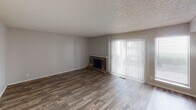 This single-floor residence offers a thoughtfully arranged layout with a comfortable blend of functional and classic design elements. The living room serves as a central highlight, featuring rich wood-look flooring, neutral gray walls, and a textured popcorn ceiling. A striking stone fireplace with a decorative herringbone-patterned accent wall anchors the space, while a large sliding glass door fitted with vertical blinds allows natural light to filter in and provides access to the outdoors.

The open-concept layout connects the living area to the dining space, which flows seamlessly toward the kitchen. The dining and entry area is outfitted with matching wood-look flooring and a ceiling fan, with a glimpse of the kitchen's cabinetry and appliances visible through an open passageway. The front entry includes closet storage and a window that brings in additional daylight.

The bedroom is a calm retreat, finished with plush carpeting and neutral tones, bathed in natural light from a side window. The bathroom is well-appointed with a white vanity featuring a granite-style countertop, a large mirror, and a tiled shower-tub combination, complemented by wood-look flooring for a cohesive aesthetic throughout. Overall, the space presents a clean, move-in-ready environment with practical finishes and a welcoming atmosphere.