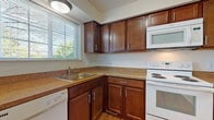 Located at 1204 Sherwood Ct in Rochester Hills, Michigan, this three-floor home offers a practical and well-organized layout across its levels. The kitchen is outfitted with rich dark-wood cabinetry, granite-toned countertops, hardwood flooring, and white Whirlpool appliances including a range, over-the-range microwave, dishwasher, and refrigerator. A window above the sink allows natural light to brighten the space. The living and dining areas feature neutral carpeting and light-toned walls, with a sliding glass door in the dining area opening to an outdoor view and allowing generous natural light. A ceiling-mounted chandelier adds a subtle decorative touch. Bedrooms are carpeted and equipped with ceiling fans, natural light from windows with outdoor views, and at least one room includes a walk-in closet with built-in shelving. The bathroom presents a clean, functional design with tile flooring, a shower-tub combo, and a dark-wood vanity with a granite-toned countertop. The unfinished basement spans a generous open area with a painted concrete floor, white-painted walls, exposed wood-beam ceiling with visible ductwork, and small ground-level windows, offering significant potential for future customization or storage use.