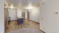 Located at 5313 W Pineridge Dr in Sioux Falls, South Dakota, this single-floor residence offers a functional and well-appointed layout designed for comfortable everyday living. The open-concept main area seamlessly connects the kitchen and living room, creating an inviting and versatile space. The kitchen features a peninsula with a built-in sink, dark cabinetry with sleek hardware, light countertops, and a full suite of black appliances including a refrigerator, electric range, and over-the-range microwave. Pendant lighting above the peninsula and a chandelier in the dining area add a warm, decorative touch. The living area is finished with plush carpeting and a ceiling fan, while durable hardwood-style flooring extends through the kitchen and entry. A bedroom offers a large window with horizontal blinds, allowing natural light to fill the room. The bathroom is equipped with a full tub and shower combo with clean white surrounds and chrome fixtures. A dedicated laundry room houses a full-size washer and dryer with overhead shelving for added storage. The layout, as seen in the dollhouse view, is efficiently organized with clear separation between living, sleeping, and utility areas.