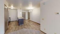 Located at 5313 W Pineridge Dr in Sioux Falls, South Dakota, this single-floor residence offers a functional and well-appointed layout designed for comfortable everyday living. The open-concept main area seamlessly connects the kitchen and living room, creating an inviting and versatile space. The kitchen features a peninsula with a built-in sink, dark cabinetry with sleek hardware, light countertops, and a full suite of black appliances including a refrigerator, electric range, and over-the-range microwave. Pendant lighting above the peninsula and a chandelier in the dining area add a warm, decorative touch. The living area is finished with plush carpeting and a ceiling fan, while durable hardwood-style flooring extends through the kitchen and entry. A bedroom offers a large window with horizontal blinds, allowing natural light to fill the room. The bathroom is equipped with a full tub and shower combo with clean white surrounds and chrome fixtures. A dedicated laundry room houses a full-size washer and dryer with overhead shelving for added storage. The layout, as seen in the dollhouse view, is efficiently organized with clear separation between living, sleeping, and utility areas.