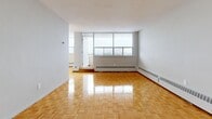 This 1-bedroom, 1-bathroom unit is thoughtfully organized across a single floor, offering a practical and comfortable layout. The spacious living room is a standout feature, showcasing warm parquet flooring in a classic herringbone-style pattern that extends throughout the main living areas and bedroom. Large floor-to-ceiling windows flood the living room with natural light while framing expansive city views, and baseboard heating units line the perimeter for year-round comfort. A balcony door provides direct outdoor access from the living space.

The kitchen is functional and well-equipped, featuring grey cabinetry with ample upper and lower storage, granite-style countertops, a double sink, and a white electric range. Light-toned ceramic tile flooring completes the kitchen's clean, practical aesthetic.

The bedroom is a comfortable size, offering built-in closet storage and the same warm parquet flooring seen throughout the unit. A window brings in natural light and additional city views, with baseboard heating ensuring warmth throughout the season.

The bathroom is bright and clean, outfitted with a full soaker tub, white subway tile surround, a pedestal sink, and neutral floor tiles. A central hallway connects all rooms efficiently, lending the unit a coherent and easy-to-navigate flow.