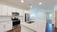 This single-floor residence showcases a thoughtfully designed open layout that seamlessly connects the kitchen and living areas. The kitchen serves as a central highlight, featuring a large island with light granite countertops, an undermount sink with a pull-down faucet, and contrasting dark cabinetry on the island base paired with crisp white upper cabinets. A classic white subway tile backsplash complements the stainless steel appliance suite, which includes a range, microwave, refrigerator, and dishwasher. Rich hardwood-style flooring runs throughout the main living and kitchen areas, adding warmth and visual continuity.

The bedrooms are finished with neutral-toned carpet and ceiling fans, contributing to a comfortable atmosphere. Each room benefits from natural light through blinded windows, with views of surrounding greenery. A walk-in closet is accessible from the primary bedroom, which also connects to an en-suite bath. The primary bathroom features a double-sink vanity with granite countertops, white shaker-style cabinetry, and a large framed mirror. A secondary bathroom offers a tub-shower combination with white tile surround and hardwood-style flooring, maintaining consistent design quality throughout the space.
