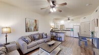 Located at 1367 N Merion Way in Fayetteville, Arkansas, this one-bedroom, two-bathroom unit offers a well-designed single-floor layout that maximizes every square foot. The open-concept living and kitchen area serves as the heart of the home, with warm wood-style flooring running throughout and ceiling fans overhead providing comfort year-round. Natural light filters in through large windows with blinds in the living room, which offers generous seating space and a wall-mounted TV setup. The kitchen is thoughtfully equipped with white cabinetry, a dark granite-style peninsula countertop with bar seating, a full suite of white appliances including a refrigerator, range, microwave, and dishwasher, and ample storage including multiple closets nearby. A dedicated dining area sits adjacent to the kitchen. The bedroom features plush carpeting, a ceiling fan, natural light from a large window, and a wall-mounted TV. Two full bathrooms serve the unit, one of which includes a tub-shower combination with a sliding glass door and a vanity with white cabinetry. The space maintains a clean, neutral palette throughout, creating a bright and functional living environment.
