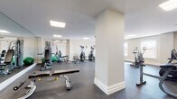 Located at 29 Linden St in Hackensack, New Jersey, this fitness center offers a well-organized and fully equipped space designed to support a wide variety of workout routines. The facility is spread across a single floor and is divided into distinct workout zones, each tailored to specific types of exercise.

The main area features multiple cardio machines, including treadmills and elliptical trainers, arranged to allow comfortable spacing between users. A dedicated strength training section houses a cable/pulley multi-function machine, a stationary bike, a Roman chair, and a dumbbell rack with a full range of weights. An adjustable workout bench and weight equipment are also available for free weight exercises.

A separate, mirrored room provides additional space for individual training, featuring a flat bench and dumbbell rack reflected in a large floor-to-ceiling mirror that enhances the sense of space. Another windowed area benefits from natural light streaming through two windows, accommodating a treadmill and air resistance bike.

Throughout the facility, durable rubber flooring provides safety and comfort during exercise. Recessed panel lighting ensures consistent, bright illumination across all zones. Wall-mounted air conditioning units maintain a comfortable climate year-round. The clean white and neutral walls contribute to a professional, focused atmosphere suited for effective training.