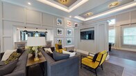 This single-floor clubhouse facility is thoughtfully designed to serve as a refined community gathering space, offering a variety of distinct areas united by a cohesive upscale aesthetic. The grand entrance immediately impresses with soaring ceilings, oversized black ironwork French doors, arched transom windows, and a bold black-and-white checkered tile floor that sets an elegant tone throughout. Large globe pendant lights illuminate the expansive lobby, which features multiple seating arrangements and opens into the broader common areas.

The lounge area is appointed with coffered tray ceilings accented by subtle ambient lighting, wainscoting wall panels, and a curated gallery wall of framed artwork. Plush charcoal sofas are paired with bold mustard-yellow accent chairs, creating a striking contrast against the neutral palette. A wall-mounted flat-screen television is seamlessly integrated into the paneling.

Adjacent, a dining and social room features deep navy walls, high ceilings, and a built-in bar with bar-stool seating, pendant lighting, and a wall-mounted display screen. A dedicated conference room offers a textured accent wall, a flat-screen display, and a central work table ideal for meetings.

The catering kitchen is well-appointed with navy cabinetry, white quartz countertops, wood-look tile flooring, and pendant lighting, providing practical functionality alongside polished design.