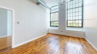 Located at 166 Valley St in Providence, Rhode Island, this single-floor loft-style unit showcases a compelling blend of historic industrial character and modern updates. Rich, original hardwood floors run throughout the entire space, anchoring the open layout with warmth and texture. Soaring ceilings amplify the sense of spaciousness, while exposed ductwork and structural columns pay homage to the building's industrial origins.

The open-concept living and kitchen area is a standout feature, with the kitchen offering light wood cabinetry, granite countertops, stainless steel appliances including a gas range, microwave, and refrigerator, and a peninsula that separates it from the main living space. A pendant light adds a touch of refinement to the kitchen area.

The bedrooms feature white-painted exposed brick walls and large, multi-pane arched factory windows that flood the rooms with natural light and frame views of the surrounding neighborhood. A walk-in closet provides generous storage.

Two bathrooms serve the unit: a full bath with tile flooring, a tub-shower combination, and a granite-topped vanity, and a half bath with a pedestal sink and round mirror. The overall ambiance is an inviting fusion of raw, historic loft aesthetics and contemporary finishes.