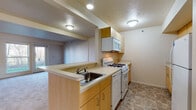 This traditional 2-bedroom, 2-bathroom residence is laid out across a single floor, offering a practical and comfortable living environment. The kitchen is efficiently designed with light wood cabinetry, a peninsula with a built-in sink, gas range, dishwasher, over-the-range microwave, and a full-size refrigerator. Stone-tile-style flooring runs throughout the kitchen, providing a clean and durable surface. The living area features neutral-toned carpet and benefits from natural light streaming through a sliding glass door that opens to the outdoors, offering views of surrounding greenery. Both bedrooms are carpeted and well-sized, each with large windows that invite natural light — one overlooks a wooded backdrop, the other faces the surrounding neighborhood. One bedroom includes a built-in closet with double rods for ample storage. The two bathrooms are consistently finished with light wood vanities, solid-surface countertops, and medicine cabinet mirrors. One bathroom features a walk-in shower, while the other offers a tub-shower combination. The overall aesthetic is clean and neutral, with a traditional design sensibility throughout.