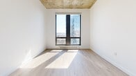 Located on Boulevard René-Lévesque Ouest in the heart of Montréal, this two-bedroom, one-bathroom unit offers a modern urban aesthetic defined by a striking combination of exposed concrete ceilings and crisp white walls throughout. Light wood laminate flooring runs continuously across the space, lending warmth and visual cohesion to every room.

The kitchen is efficiently designed with white cabinetry, a classic square-tile backsplash, and a built-in range hood, opening toward the hallway and living area for a connected feel. The living area benefits from floor-to-ceiling windows that frame sweeping city views and flood the space with natural light.

Both bedrooms continue the industrial-modern theme with exposed concrete ceilings and large windows that invite abundant daylight and impressive urban panoramas. The primary bedroom includes a closet and a wall-mounted air conditioning unit for year-round comfort. The second bedroom features its own closet with a built-in rod for convenient storage.

The bathroom is finished with full square-tile walls and floors, a sleek white floating vanity, and a glass-enclosed shower, offering a clean and functional design. A well-proportioned hallway connects all rooms, completing this thoughtfully laid-out urban residence in one of Montréal's most vibrant corridors.