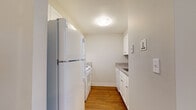 Located at 109 Riverboat Village Rd in South Hadley, Massachusetts, this single-floor residence offers a straightforward and functional layout highlighted by warm hardwood flooring that runs consistently throughout the space. The open living area is bright and simply designed, featuring neutral gray walls, clean white trim, and a pass-through window that connects directly to the kitchen, creating a sense of openness between the two spaces.

The kitchen is efficiently arranged in a galley-style configuration, featuring white cabinetry with granite-patterned countertops, a white refrigerator, range, and sink. Upper and lower cabinets provide ample storage within the compact footprint, keeping everything organized and accessible.

The bedroom is well-proportioned, offering natural light through a pair of windows that look out toward greenery. A baseboard heating unit runs along the exterior wall, and a closet with a rod and shelf provides convenient storage. The room connects easily to the rest of the unit through a paneled white door.

The bathroom is clean and straightforward, with a white vanity cabinet, an integrated sink, a wall mirror with overhead lighting, and a tub-shower combination. Hardwood flooring continues into this space, maintaining a cohesive look throughout the unit. Overall, the space presents a tidy, no-frills aesthetic well-suited for comfortable, everyday living.