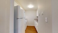 Located at 109 Riverboat Village Rd in South Hadley, Massachusetts, this single-floor residence offers a straightforward and functional layout highlighted by warm hardwood flooring that runs consistently throughout the space. The open living area is bright and simply designed, featuring neutral gray walls, clean white trim, and a pass-through window that connects directly to the kitchen, creating a sense of openness between the two spaces.

The kitchen is efficiently arranged in a galley-style configuration, featuring white cabinetry with granite-patterned countertops, a white refrigerator, range, and sink. Upper and lower cabinets provide ample storage within the compact footprint, keeping everything organized and accessible.

The bedroom is well-proportioned, offering natural light through a pair of windows that look out toward greenery. A baseboard heating unit runs along the exterior wall, and a closet with a rod and shelf provides convenient storage. The room connects easily to the rest of the unit through a paneled white door.

The bathroom is clean and straightforward, with a white vanity cabinet, an integrated sink, a wall mirror with overhead lighting, and a tub-shower combination. Hardwood flooring continues into this space, maintaining a cohesive look throughout the unit. Overall, the space presents a tidy, no-frills aesthetic well-suited for comfortable, everyday living.
