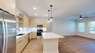 This well-designed single-floor residence offers a thoughtful layout encompassing a bedroom, bathroom, kitchen and living area, dedicated laundry room, and closet. The open-concept kitchen and living space serves as the heart of the home, showcasing light wood flat-panel cabinetry that extends floor to ceiling, crisp white quartz countertops, a white subway tile backsplash, and a suite of stainless steel appliances including a range, built-in microwave, dishwasher, and refrigerator. A central island with pendant lighting adds both function and style, while warm wood-look luxury vinyl plank flooring flows seamlessly throughout the entire residence. The living area benefits from natural light through multiple windows fitted with horizontal blinds and includes a ceiling fan for added comfort. The bedroom is a well-proportioned retreat with outdoor views through bright, sunlit windows and its own ceiling fan. The bathroom features a soaking tub with a subway-tiled surround, matte black fixtures and hardware, and clean white finishes. A dedicated laundry room houses a full-size front-load washer and dryer with overhead shelving. Recessed lighting and crisp white walls contribute to a bright, contemporary ambiance throughout.