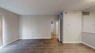 This single-floor residential unit offers a well-organized layout designed for comfortable everyday living. The main living area is anchored by rich, dark hardwood-style flooring and neutral gray walls, creating a clean and contemporary aesthetic throughout. A front entry door opens directly into the open living space, where a pass-through counter separates the living area from the kitchen, providing a connected yet defined layout.

The kitchen is efficiently designed in a galley configuration, featuring white cabinetry with brushed nickel hardware, a herringbone tile backsplash, stone-look countertops, a deep single-basin sink with a modern pull-down faucet, and black appliances including an electric range and refrigerator. Light wood-tone flooring in the kitchen complements the white cabinetry for a bright, cohesive finish.

The bedroom is carpeted with plush neutral-toned carpet and benefits from dual windows fitted with white blinds, allowing for ample natural light. A ceiling fan with integrated lighting adds both comfort and functionality to the space.

Additional areas include a secondary room with dark hardwood-style flooring and a large vertical-blind window that lets in generous natural light. The bathroom is finished with a granite-look vanity countertop, white cabinetry, textured walls, and a full tub-shower combination. Overall, the unit presents a refreshed, move-in ready interior with consistent modern finishes throughout.