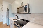 Located at 715 E 36th St in Charlotte, NC, this thoughtfully designed single-floor unit offers a clean, modern aesthetic throughout. Light hardwood flooring flows seamlessly across the entire space, complementing the bright white walls and creating a warm, cohesive feel.

The kitchen is a standout feature, showcasing soft sage-toned cabinetry with matte black hardware, white quartz countertops, and a classic subway tile backsplash. Stainless steel appliances — including an electric range, over-the-range microwave, and refrigerator — provide full functionality, while a single-basin sink with a matte black faucet adds a modern touch.

The open living area benefits from recessed lighting and connects effortlessly to the kitchen, maximizing the sense of space. A set of French doors opens to a private balcony, inviting abundant natural light and outdoor views. Adjacent to the living area is a dedicated walk-in closet, offering practical storage solutions.

The full bathroom features a clean, minimalist design with a shower-tub combination and matte black fixtures consistent with the overall design language. An entrance area and additional closet space complete the layout. The unit's design prioritizes smart use of space, modern finishes, and a bright, airy ambiance throughout.