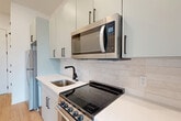 Located at 715 E 36th St in Charlotte, NC, this thoughtfully designed single-floor unit offers a clean, modern aesthetic throughout. Light hardwood flooring flows seamlessly across the entire space, complementing the bright white walls and creating a warm, cohesive feel.

The kitchen is a standout feature, showcasing soft sage-toned cabinetry with matte black hardware, white quartz countertops, and a classic subway tile backsplash. Stainless steel appliances — including an electric range, over-the-range microwave, and refrigerator — provide full functionality, while a single-basin sink with a matte black faucet adds a modern touch.

The open living area benefits from recessed lighting and connects effortlessly to the kitchen, maximizing the sense of space. A set of French doors opens to a private balcony, inviting abundant natural light and outdoor views. Adjacent to the living area is a dedicated walk-in closet, offering practical storage solutions.

The full bathroom features a clean, minimalist design with a shower-tub combination and matte black fixtures consistent with the overall design language. An entrance area and additional closet space complete the layout. The unit's design prioritizes smart use of space, modern finishes, and a bright, airy ambiance throughout.