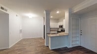 This single-floor residence is thoughtfully designed with a blend of modern finishes and classic architectural details. The open-concept layout connects the kitchen and living areas seamlessly, with wood-look flooring extending throughout the main spaces and crown molding adding a refined touch to the ceilings.

The kitchen is well-appointed with crisp white cabinetry, a subway tile backsplash, granite countertops, and a full suite of stainless steel appliances, including a refrigerator, range, and microwave. A peninsula with a built-in sink provides additional prep space and serves as a natural divider between the kitchen and the adjoining living area. Built-in shelving adds practical storage nearby.

The living room is a standout feature, boasting large windows that invite ample natural light and a classic fireplace with a white-painted mantel as its focal point. The bedroom offers plush carpeting, a ceiling fan, natural light from a window, and access to a closet.

The bathroom is finished with granite countertops on a grey vanity, a large mirror, and a soaking tub with distinctive red tile accents set against white tile surround. Wood-look flooring carries through into the bathroom, maintaining a cohesive aesthetic throughout the space.