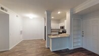 This single-floor residence is thoughtfully designed with a blend of modern finishes and classic architectural details. The open-concept layout connects the kitchen and living areas seamlessly, with wood-look flooring extending throughout the main spaces and crown molding adding a refined touch to the ceilings.

The kitchen is well-appointed with crisp white cabinetry, a subway tile backsplash, granite countertops, and a full suite of stainless steel appliances, including a refrigerator, range, and microwave. A peninsula with a built-in sink provides additional prep space and serves as a natural divider between the kitchen and the adjoining living area. Built-in shelving adds practical storage nearby.

The living room is a standout feature, boasting large windows that invite ample natural light and a classic fireplace with a white-painted mantel as its focal point. The bedroom offers plush carpeting, a ceiling fan, natural light from a window, and access to a closet.

The bathroom is finished with granite countertops on a grey vanity, a large mirror, and a soaking tub with distinctive red tile accents set against white tile surround. Wood-look flooring carries through into the bathroom, maintaining a cohesive aesthetic throughout the space.