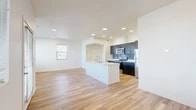 Located at 2525 S Meadows Rd in Santa Fe, NM, this thoughtfully designed single-story home offers three bedrooms and two bathrooms across a well-utilized floor plan. The heart of the home is an open-concept living, dining, and kitchen area that flows seamlessly together, bathed in natural light from multiple windows offering neighborhood views. The kitchen is a standout feature, showcasing a large central island with a built-in sink and white countertops, bold dark cabinetry with tile backsplash, and stainless steel appliances including a range, microwave, and refrigerator. Warm-toned light wood flooring runs throughout the entire home, lending a clean, cohesive aesthetic. The living area provides direct access to a private balcony through a glass door, extending the living space outdoors. The three bedrooms are well-proportioned and bright, with the primary bedroom offering generous closet space. Four closets throughout the home ensure ample storage. The two bathrooms are finished with dark vanity cabinetry and white countertops; one features a full soaking tub and shower combination. A dedicated laundry area and hallway complete the functional layout of this contemporary Santa Fe residence.
