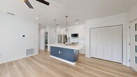 Located at 527 N Garden Ave in Clearwater, Florida, this thoughtfully designed 2-bedroom, 3-bathroom residence offers a clean, modern aesthetic across a single floor. Light-toned hardwood-style flooring flows throughout, complemented by crisp white walls and recessed lighting that create a bright, airy atmosphere.

The open-concept kitchen and living area serves as the heart of the home. The kitchen features a bold navy blue island with a white quartz countertop, an undermount sink with a modern pull-down faucet, and stylish globe pendant lights. White shaker cabinetry lines the walls alongside stainless steel appliances, including a French door refrigerator, range, and built-in microwave. The adjacent living area benefits from multiple windows that invite natural light and ceiling fans for added comfort.

Both bedrooms are generously proportioned, with the primary bedroom offering direct access to a private balcony through sliding glass doors, providing pleasant outdoor views. The second bedroom also features exterior door access and its own ceiling fan. Three closets, including louvered double-door designs, provide ample storage throughout.

All three bathrooms are finished with floor-to-ceiling marble-style tile, navy vanities with gold hardware, and glass-enclosed showers. A dedicated laundry area and a hallway connecting the main spaces round out this well-appointed home.