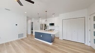 Located at 527 N Garden Ave in Clearwater, Florida, this thoughtfully designed 2-bedroom, 3-bathroom residence offers a clean, modern aesthetic across a single floor. Light-toned hardwood-style flooring flows throughout, complemented by crisp white walls and recessed lighting that create a bright, airy atmosphere.

The open-concept kitchen and living area serves as the heart of the home. The kitchen features a bold navy blue island with a white quartz countertop, an undermount sink with a modern pull-down faucet, and stylish globe pendant lights. White shaker cabinetry lines the walls alongside stainless steel appliances, including a French door refrigerator, range, and built-in microwave. The adjacent living area benefits from multiple windows that invite natural light and ceiling fans for added comfort.

Both bedrooms are generously proportioned, with the primary bedroom offering direct access to a private balcony through sliding glass doors, providing pleasant outdoor views. The second bedroom also features exterior door access and its own ceiling fan. Three closets, including louvered double-door designs, provide ample storage throughout.

All three bathrooms are finished with floor-to-ceiling marble-style tile, navy vanities with gold hardware, and glass-enclosed showers. A dedicated laundry area and a hallway connecting the main spaces round out this well-appointed home.
