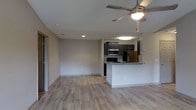 This single-floor residence features an open-concept design that seamlessly connects the living area and kitchen, creating a spacious and functional layout. Light-toned hardwood-style flooring extends throughout, lending warmth and visual continuity across the space.

The living area is well-lit with recessed lighting and a ceiling fan with an integrated light fixture, providing both ambient illumination and air circulation. Neutral-toned walls offer a clean, versatile backdrop throughout the unit.

The kitchen is defined by a peninsula with a granite-style countertop, offering additional prep space and serving as a natural divider between the kitchen and living areas. Dark espresso cabinetry provides strong visual contrast against the lighter surroundings, while stainless steel appliances — including a microwave and refrigerator — add a modern touch. The kitchen also benefits from its own overhead lighting fixture. A sliding door visible near the living area suggests access to an outdoor space or additional room, adding further utility to this well-appointed single-level residence.
