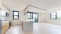 Located at 440 Elizabeth Ave in Newark, NJ, this thoughtfully designed 4-bedroom, 2-bathroom residence offers a seamless blend of modern aesthetics and functional living across a single floor. The open-concept kitchen and living area serves as the heart of the home, anchored by a striking marble-veined waterfall island with a matte black faucet and warm wood-paneled base. White upper cabinetry, a marble tile backsplash, stainless steel appliances, and a bold black track lighting system complete the kitchen. Oversized black-framed windows and a sliding glass door flood the living area with natural light and provide outdoor views. Light-toned hardwood-style flooring flows consistently throughout the unit, enhancing its bright, airy feel. The four bedrooms are well-proportioned and serene, featuring clean white walls and generous closet space, including a walk-in closet with a full rod system and a primary bedroom with a floor-to-ceiling built-in wardrobe wall in slate gray. Both bathrooms are stylishly finished — one with earthy green ceramic tile surrounding the tub and a wood-toned vanity, the other with large-format gray tile flooring and a navy vanity — both featuring LED-backlit mirrors and oil-rubbed bronze fixtures.