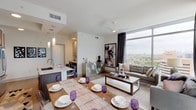 This thoughtfully designed two-bedroom, two-bathroom residence offers a refined urban living experience highlighted by dramatic floor-to-ceiling windows that frame sweeping city skyline views. The open-concept main living area seamlessly connects the kitchen, dining, and living spaces, creating a cohesive and functional layout ideal for both everyday living and entertaining.

The kitchen is appointed with quartz countertops, a generous island with an undermount sink, stainless steel appliances including a double oven and French door refrigerator, and a combination of white upper cabinetry and rich dark wood lower cabinets. Pendant lighting adds a polished finishing touch overhead.

The living room benefits from corner window placement, flooding the space with natural light and providing panoramic city views. The dining area comfortably accommodates a full-size table adjacent to the kitchen.

Both bedrooms offer large windows with city vistas. The primary bedroom features a moody accent wall and pendant lighting, while the second bedroom showcases a bold artistic wall mural. Each bathroom is well-appointed with marble-style quartz vanities and tile surrounds. The primary bath includes both a soaking tub and a separate glass-enclosed shower.