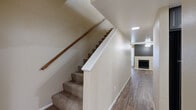 This two-story home is efficiently designed across two floors, with the ground floor housing the main living areas and the upper floor dedicated primarily to bedrooms. The ground floor features an open-plan living room and kitchen layout. The living room is finished with wood-look vinyl flooring, a ceiling fan, and a tiled fireplace framed by a bold dark accent wall, adding a focal point to the space. Vertical blinds provide access to natural light. The kitchen is equipped with dark-toned cabinetry, light stone countertops, black appliances including a gas range, microwave, and refrigerator, and connects seamlessly to the living area via a pass-through counter. A bathroom on this floor includes a dark wood vanity with stone countertops and mirrored cabinet. Carpeted stairs with a wood handrail lead to the upper floor, where the bedrooms are located. Each bedroom features neutral carpet, textured ceilings, and sliding mirrored closet doors with built-in shelving. The primary bedroom includes a dedicated closet. Bathrooms feature white tub-shower combinations with clean, simple finishes throughout.