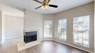 This well-appointed single-floor residence in Dallas, Texas offers a thoughtful layout across two bedrooms, a combined dining, kitchen, and living area, a laundry space, three closets, a hallway, and a private patio. The living room serves as the heart of the home, highlighted by a tile-surround fireplace, warm wood-look flooring, and multiple windows that flood the space with natural light. A ceiling fan overhead adds both style and comfort to the airy room. Adjacent to the living area, the dining space continues the wood-look flooring and connects seamlessly to the kitchen via a pass-through window. The galley-style kitchen is outfitted with white cabinetry, light stone countertops, a stainless steel sink, and black appliances including a refrigerator, range, and built-in microwave. The two bedrooms feature plush carpeting, ceiling fans, and textured ceilings, with the primary bedroom offering generous proportions and direct access to a closet. The second bedroom is bright, with a window inviting in natural light. A patio extends the living space outdoors, while the in-unit laundry adds everyday convenience. Neutral tones throughout create a calm, cohesive ambiance.