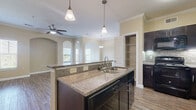 This single-floor, 2-bedroom, 2-bathroom residence in Conroe, TX offers a thoughtfully designed open-concept layout. The kitchen serves as a central highlight, featuring a large island with granite countertops, a double stainless steel sink, and elegant pendant lighting overhead. Dark espresso cabinetry pairs with a tile backsplash and black appliances, including a range, microwave, and refrigerator. A built-in pantry provides additional storage. The kitchen flows seamlessly into the living and dining areas, where arched architectural details, crown molding, and a ceiling fan enhance the space. Wood-style flooring extends throughout the main living areas, adding warmth and continuity. The primary bedroom is generously sized, featuring plush carpet, crown molding, a ceiling fan, and a window with natural light. It connects directly to a private en-suite bathroom with a glass-enclosed shower, granite vanity, dark cabinetry, and wood-style flooring. The second bedroom also features carpet flooring and ample natural light. Both bedrooms include dedicated closets with wire shelving systems. Additional conveniences include a dedicated laundry area and in-unit storage. Crown molding and neutral tones throughout create a cohesive, polished ambiance.