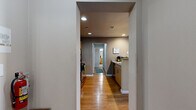 This single-floor unit is thoughtfully designed to accommodate four bedrooms and four full bathrooms within a compact but efficiently utilized footprint. Hardwood flooring runs throughout the main living areas and kitchen, contributing warmth and visual continuity across the space. Two hallways connect the rooms, providing a logical and organized flow throughout.

The living room is a welcoming space featuring a ceiling fan, neutral walls, and multiple windows that invite natural light while offering views to the exterior. The kitchen is well-appointed with light wood cabinetry, stainless steel appliances including a refrigerator, microwave, and range, granite-style countertops, and a breakfast bar that provides additional seating and casual dining options. Recessed lighting illuminates both the kitchen and connecting hallway areas.

Each of the four bedrooms is carpeted and modestly sized, accommodating a bed and desk, making them well-suited for individual use. The primary bedroom includes its own private access point. The four bathrooms are finished with tile flooring and shower-tub combinations. Overall, the unit delivers a functional, well-organized layout designed to maximize the use of every available area.
